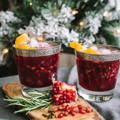 two glasses filled with pomegranate on top of a wooden cutting board next to a christmas tree