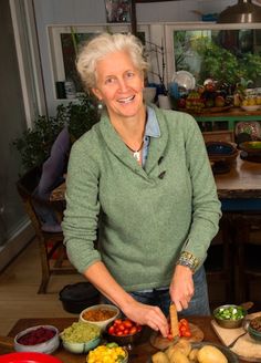 a woman standing in front of a table filled with vegetables and fruit on top of it