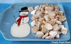 a blue plate topped with snowmen next to a pile of puppy chows covered in powdered sugar