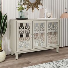 a white cabinet with glass doors and a mirror on the top, next to a potted plant