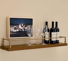 wine glasses and bottles are sitting on a shelf in front of a framed painting with a dog