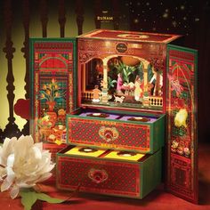 an elaborately decorated jewelry box sits next to a white flower on a red surface