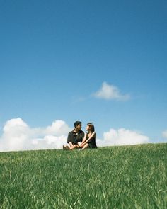 a man and woman sitting in the grass under a blue sky