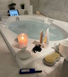 a bathtub with candles, soap and other items in it next to a laptop