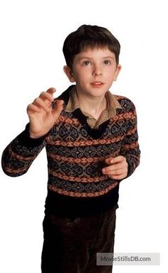 a young boy in a sweater making a hand gesture