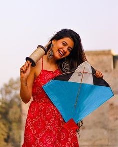 a woman in a red dress is holding a blue and black kite while smiling at the camera