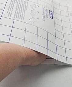 a hand holding a piece of paper on top of a white table with blue lines