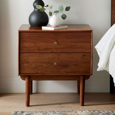 a wooden dresser with two black vases on top and a bed in the background