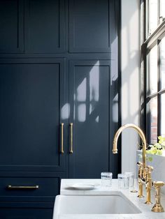 a white sink sitting under a window next to a tall cabinet with gold handles and knobs