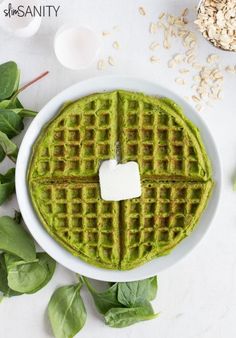 a waffle topped with green pesto on top of a white plate next to some leaves