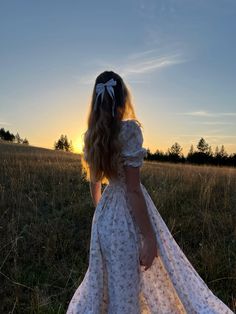 a woman in a white dress standing in a field at sunset with her back to the camera