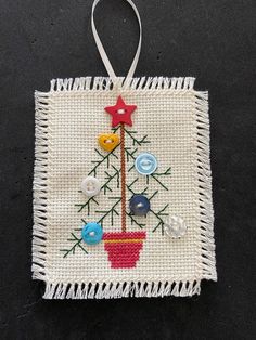 a small christmas tree ornament hanging on a black surface with white fringes