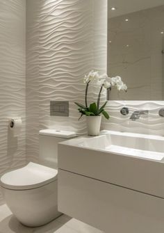 a white toilet sitting next to a sink in a bathroom under a mirror and a vase with flowers