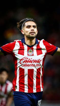 a soccer player with his arms stretched out in the air while wearing a red and white striped shirt