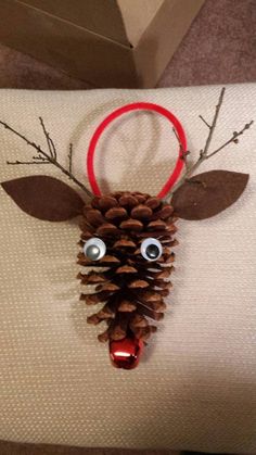 a deer head made out of pine cones on top of a white pillow with red ribbon