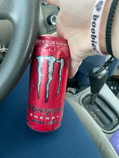 a can of monster energy drink being held by someone's hand in a car