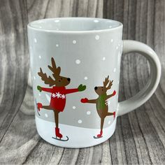 a white coffee mug with two reindeers skating on the snow and one is wearing a red sweater