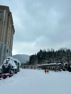 a train is parked in the snow next to a building and two people are walking by