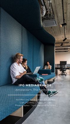 two people sitting on a blue couch using laptops