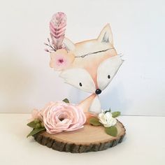 a small figurine of a fox with feathers and flowers on top of a piece of wood