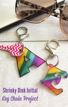 two key chains with the words shrinky pink initial and rainbow puzzle on them, next to a pair of sunglasses