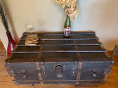 an old trunk with flowers in it on a wooden floor next to a wine glass