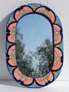 a colorful mirror hanging on the wall with trees in the backgroung behind it