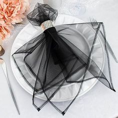 a white plate topped with black mesh on top of a table next to pink flowers