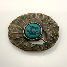 a metal object with a blue stone in the center on a white surface, it appears to be brooch or lapel