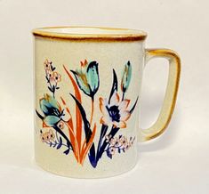 a coffee mug with flowers painted on it's side and gold trimmings