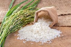 white rice is spilling out of a sack on a wooden table next to some green stalks