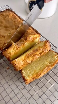 a person cutting into a cake with a knife on a cooling rack next to a cup