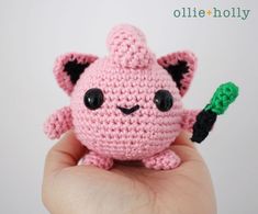 a small pink crocheted toy with black eyes holding a green object in it's hand