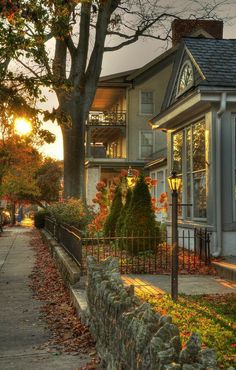 the sun is setting in front of a large house with trees and bushes around it