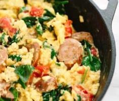 an omelet with sausages, spinach and tomatoes in a skillet