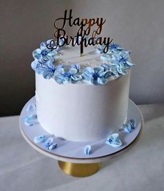 a white cake with blue flowers and a happy birthday sign on top