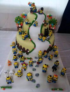 a three tiered cake decorated with minion figures and decorations on a white tablecloth