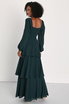 the back of a woman wearing a dark green dress with long sleeves and tiered skirt