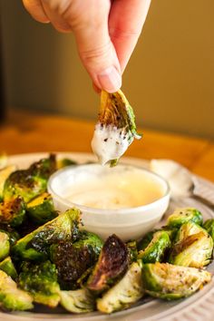 a person dipping something into a small bowl of sauce on top of a plate of vegetables