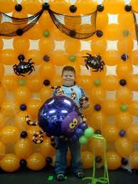 a young boy standing in front of an orange wall with balloons and spider decorations on it