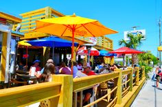 people are sitting at tables under umbrellas on the boardwalk in front of some buildings