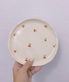 a hand holding a white plate with red cherries on the rim and green leaves