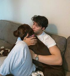 a man sitting on a couch holding a dog with his face close to the ground