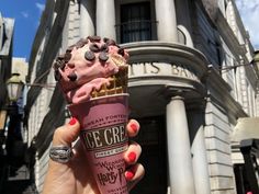 a person holding up an ice cream cone with chocolate chips on it in front of a building