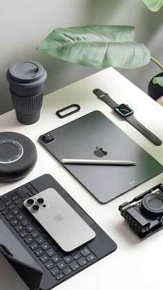 an assortment of electronics and gadgets on a white table with a green plant in the background