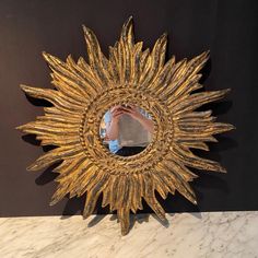 a person taking a photo of a gold sunburst mirror on a marble counter