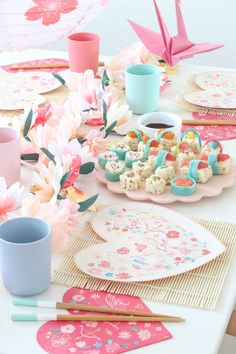 a table topped with plates and cups filled with food next to paper cranes on the wall