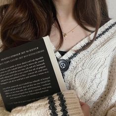 a woman is holding a book in her hands while wearing a white knitted sweater