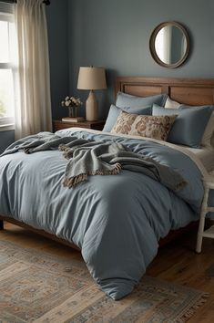 a bed with blue sheets and pillows in a bedroom next to a window on a wooden floor