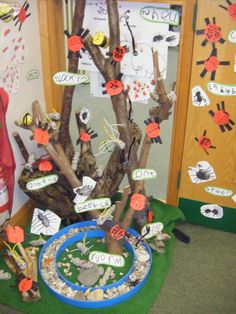 a tree made out of branches and paper with pictures on the branches, in front of a bulletin board